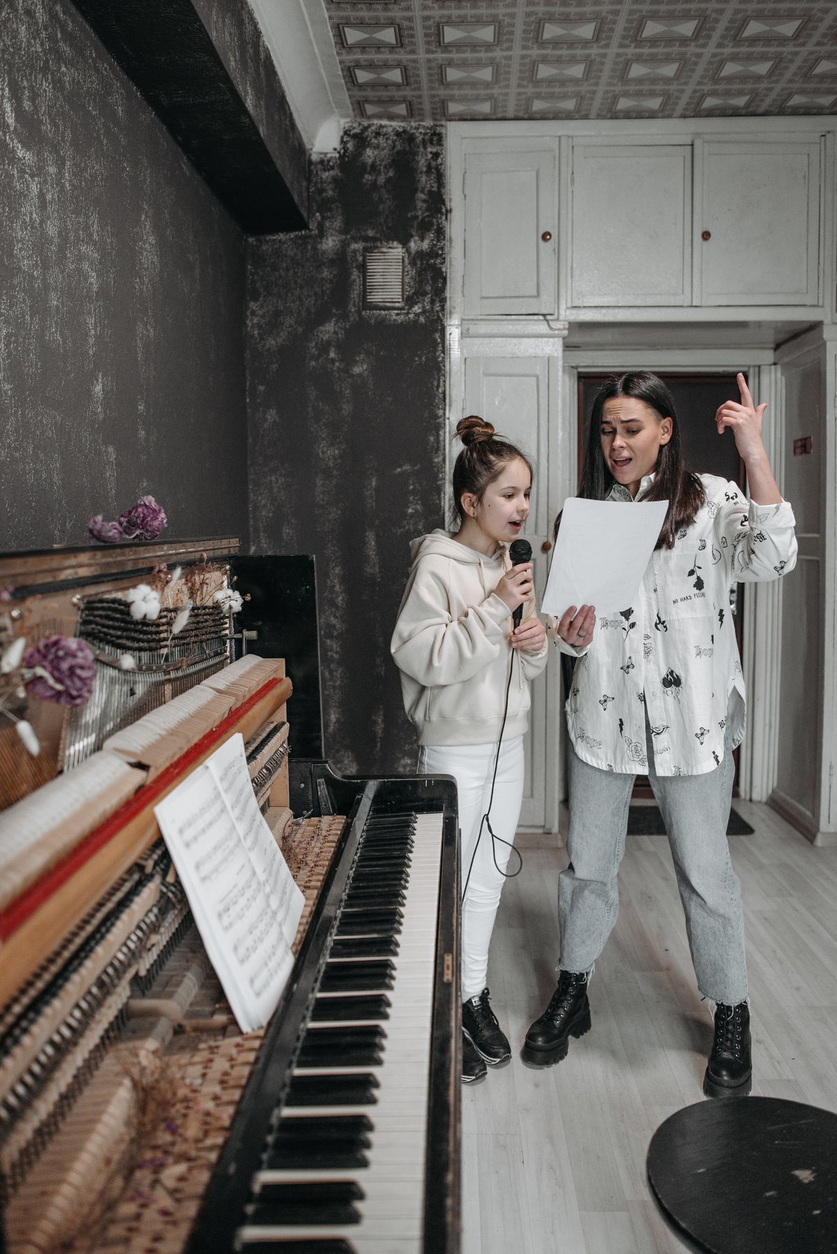 A vocal coach mid-lesson, hand raised, leading her student through the song