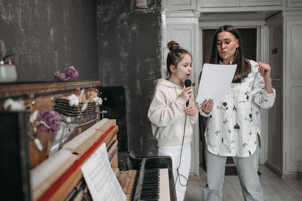 A vocal coach and her student singing together at the piano