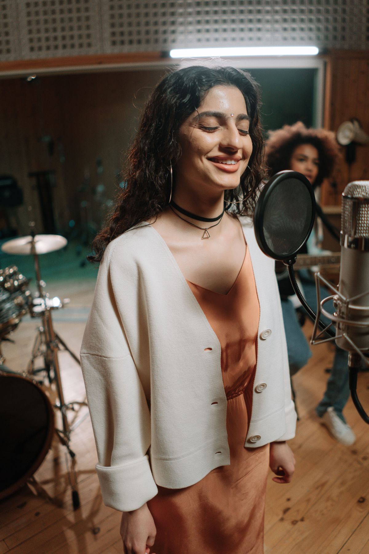 A young singer mid-practice at a studio condenser microphone, eyes closed