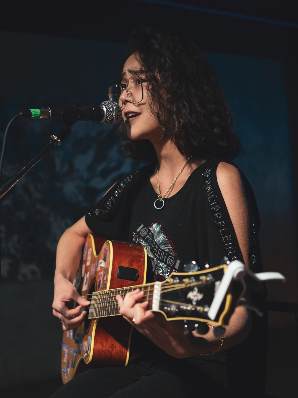 A singer finding her voice, eyes lifted, singing into the microphone with her guitar