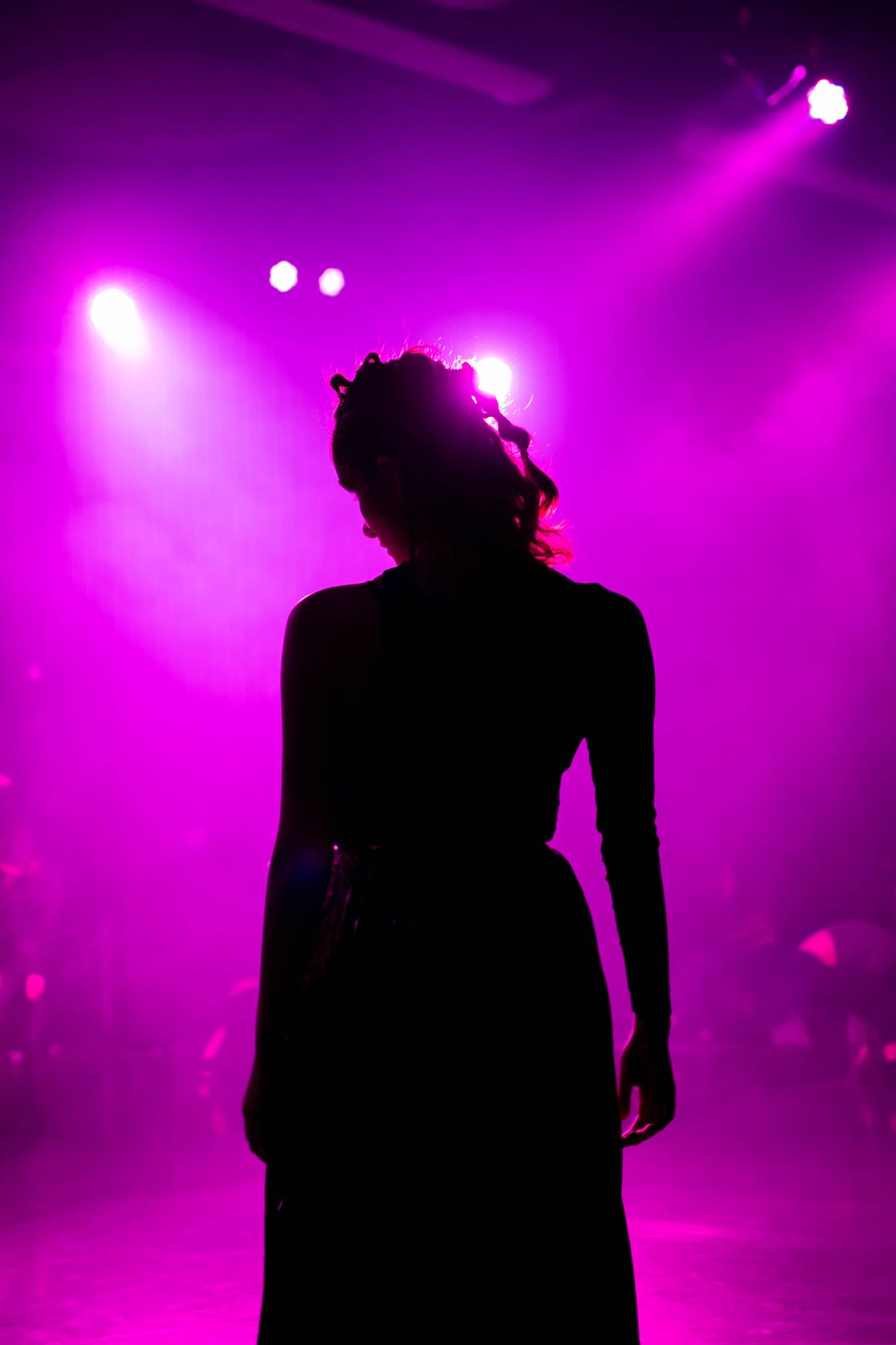 A performer from behind, facing the stage lights and owning them