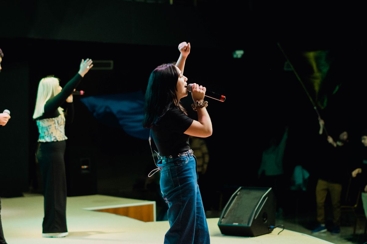 A singer at an open mic, arm raised, shaping her craft in front of the room