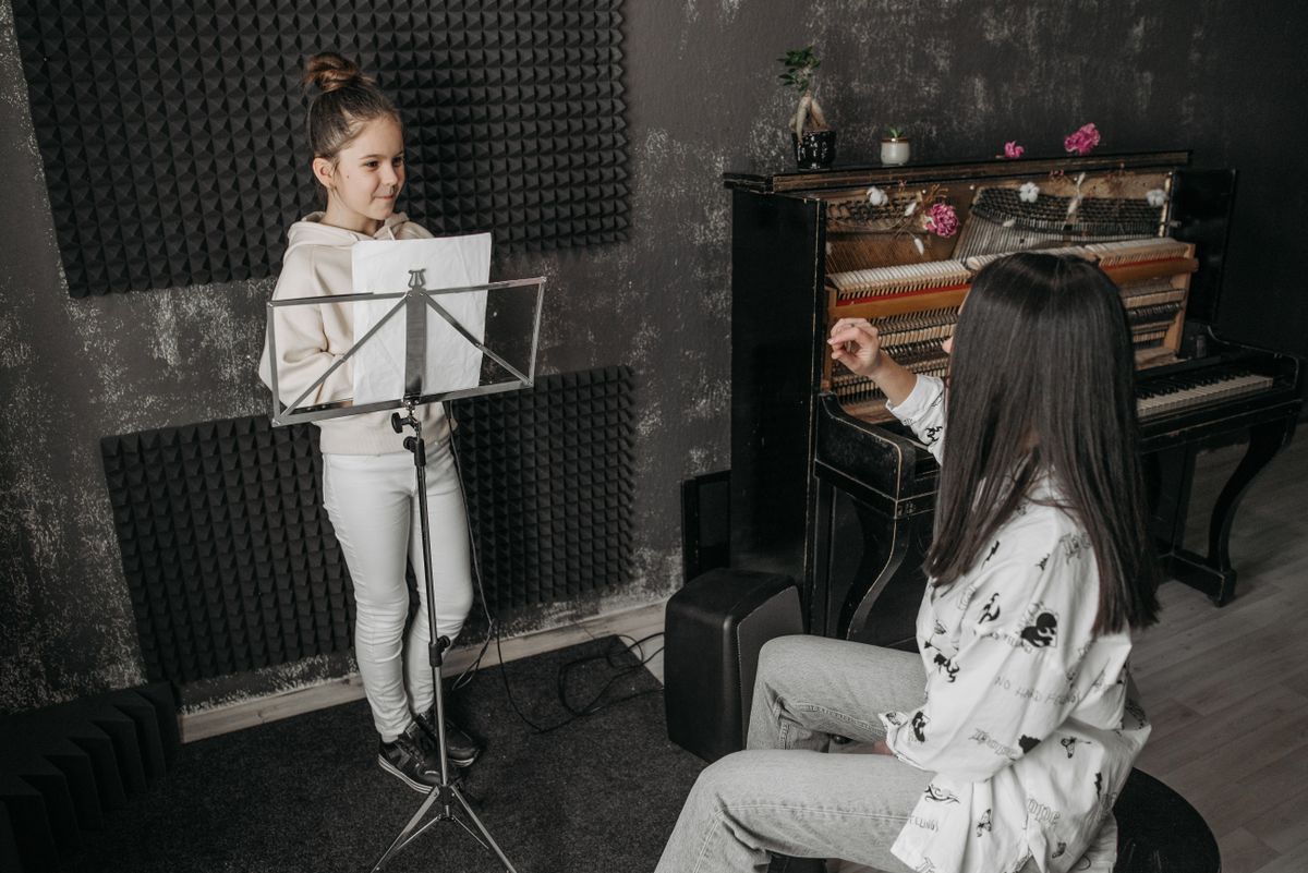 A vocal coach guiding her standing student through a singing lesson at the piano
